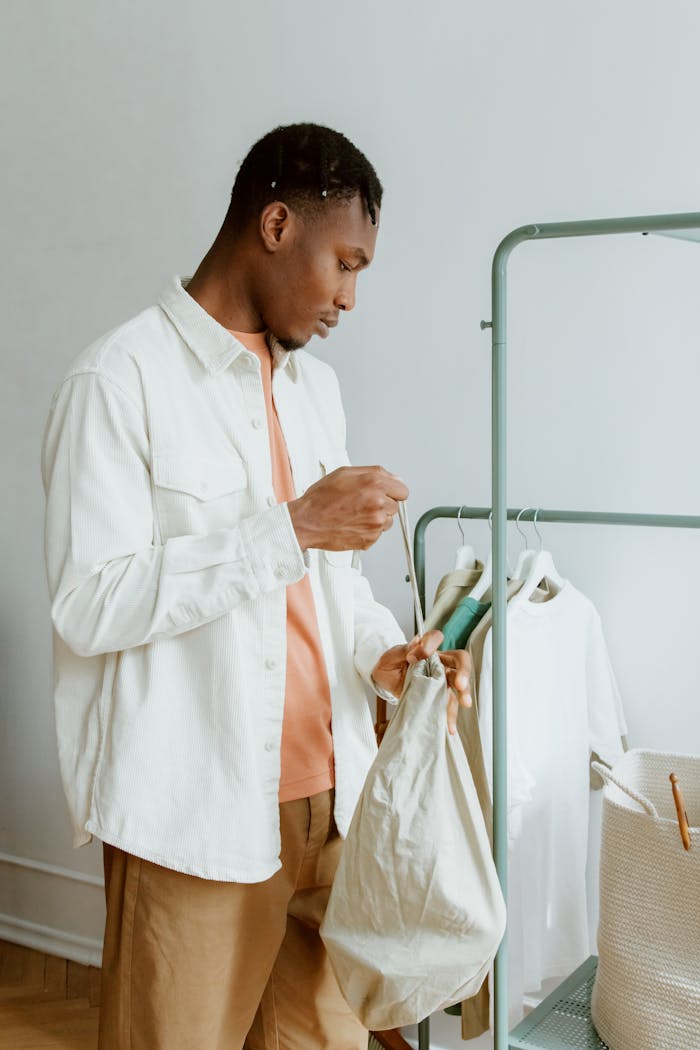 services-02 A stylish young man arranges clothes on a modern clothing rack indoors.