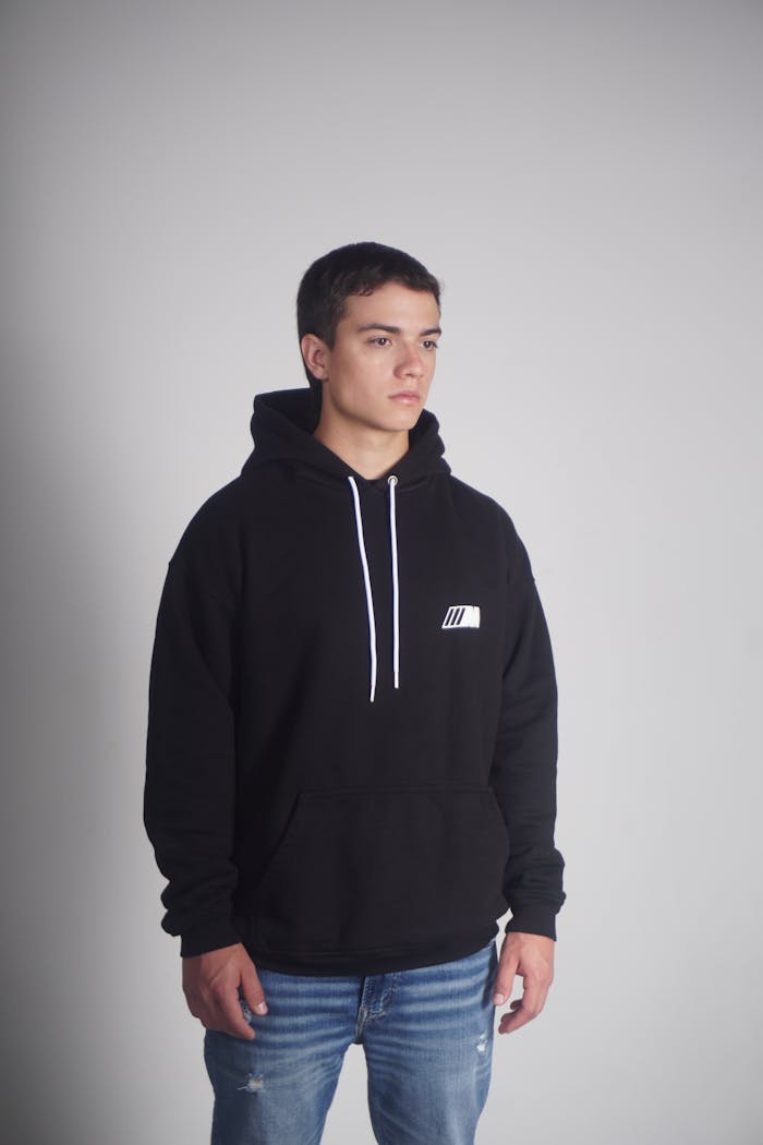 Portrait of a young man wearing a black hoodie and jeans against a gray backdrop.